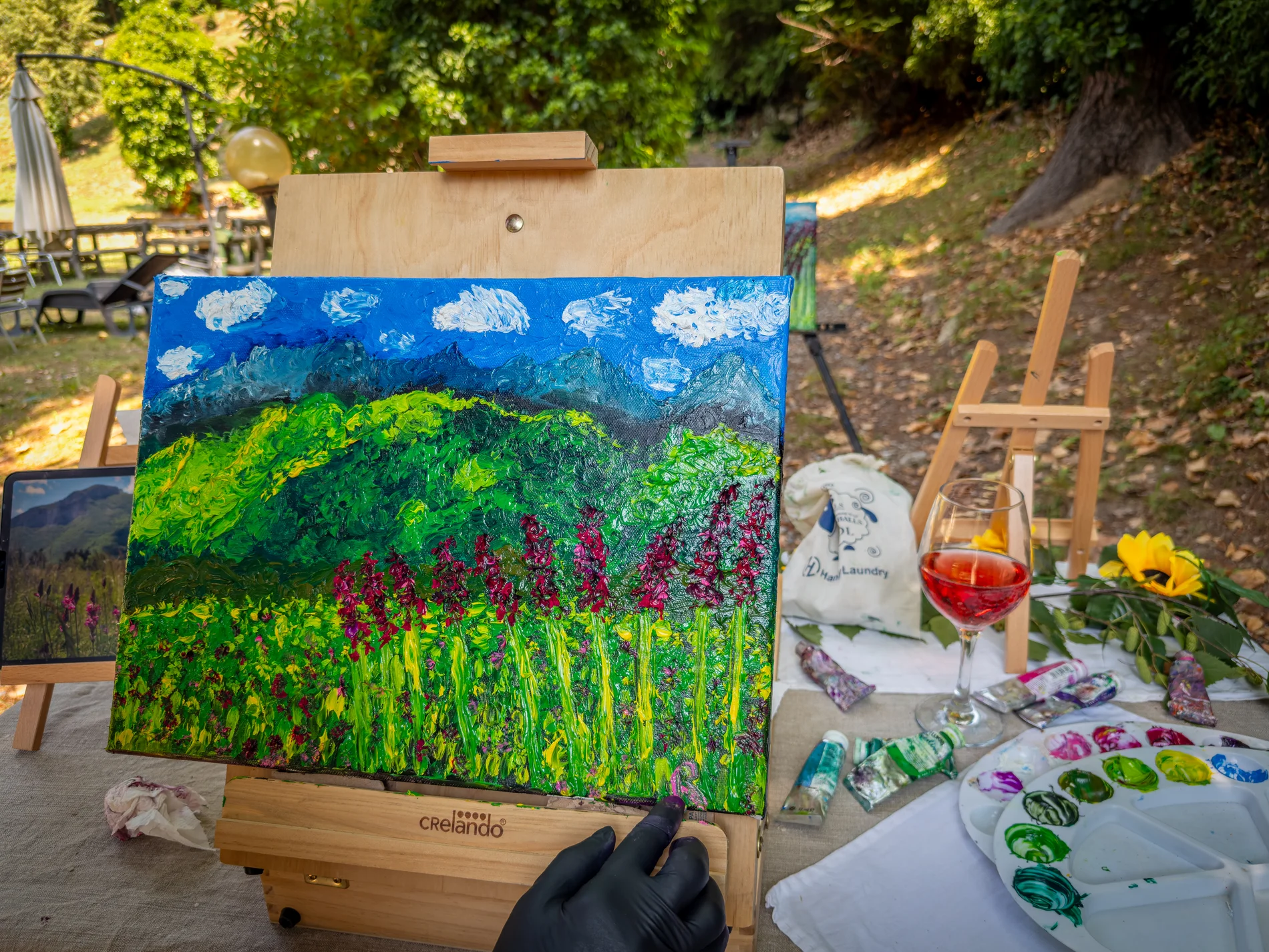 A painting on an easel with the palette and a glass of wine, in the park
